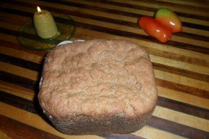 Fresh baked sprouted grain bread on cutting board with candle and tomatoes.