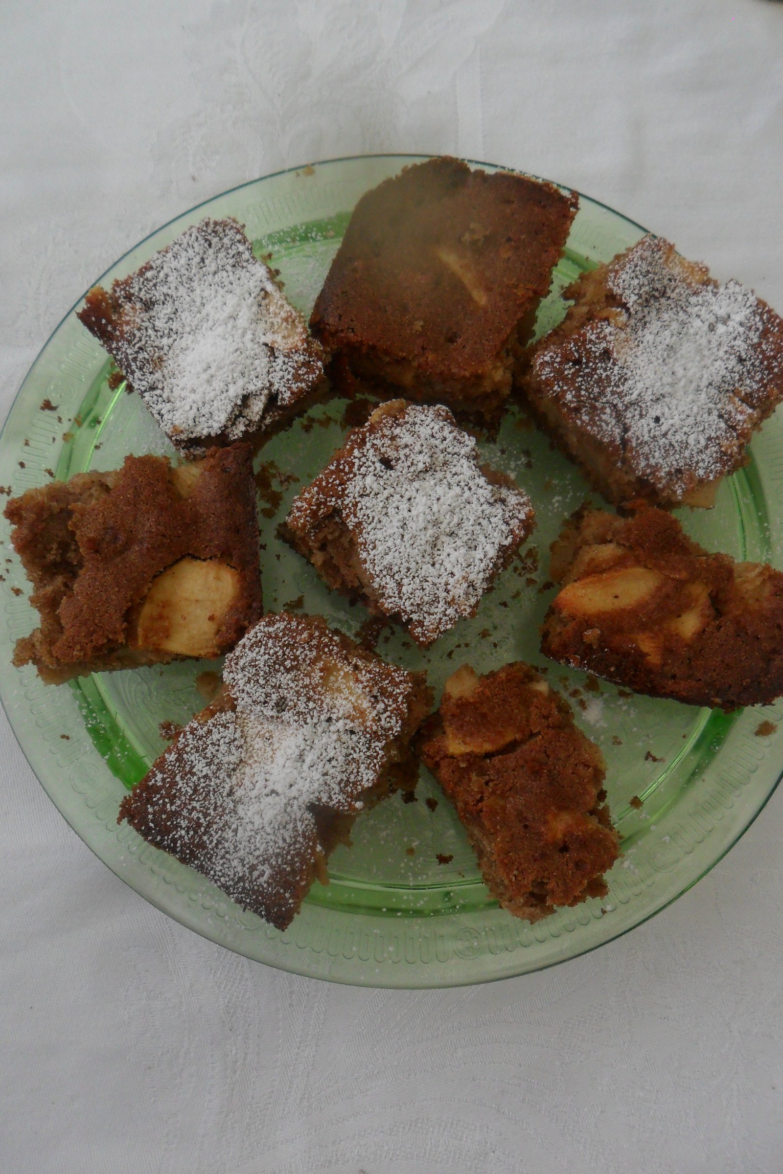 Pieces of apple cake on plate, some with powdered sugar