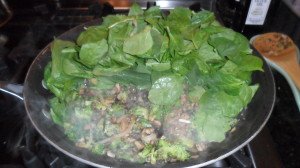 Vegetables cookiing in pan with spinach on top.