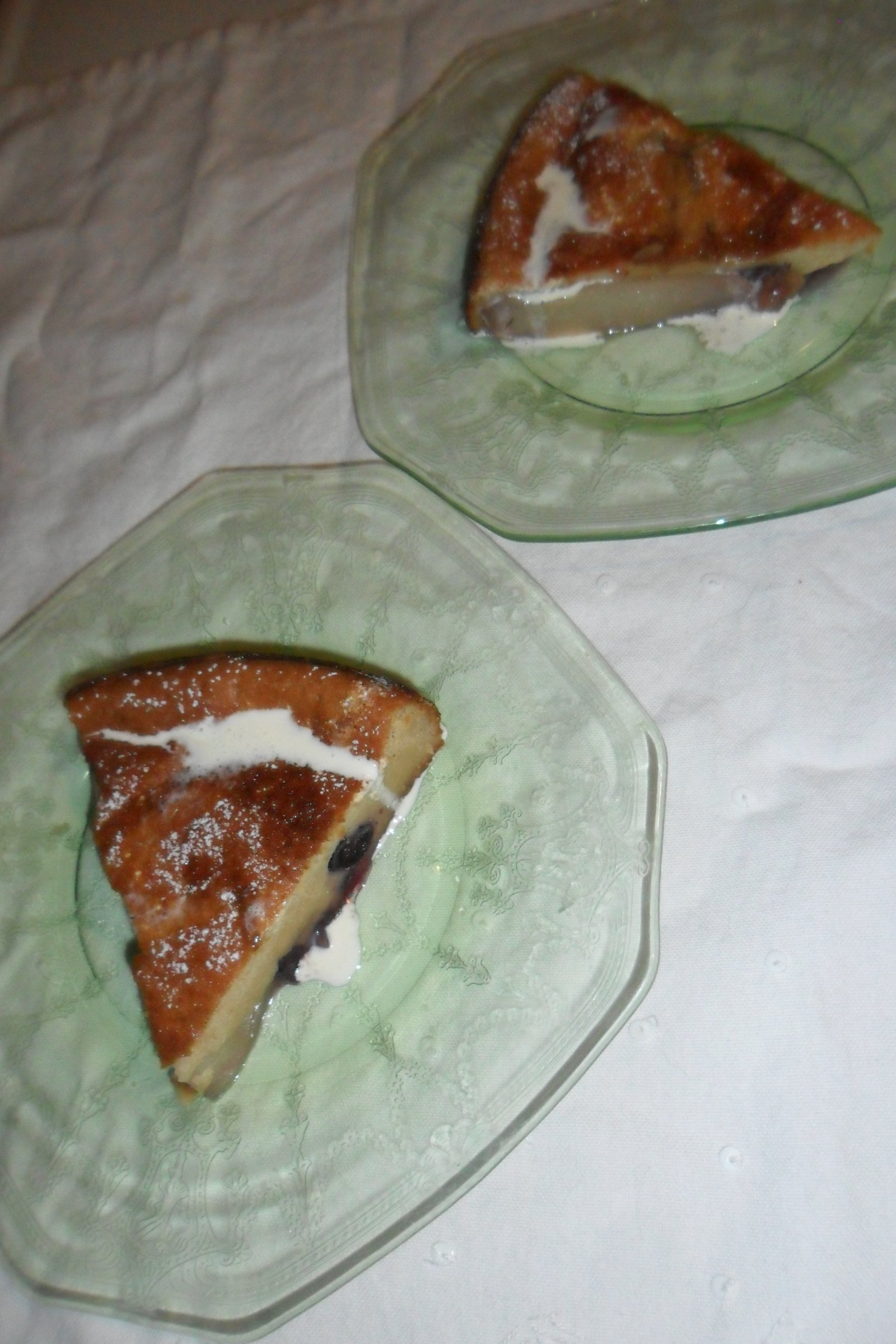 Two pieces of clafoutis on plates with cream drizzled