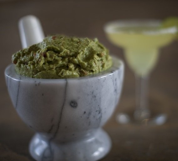 Guacamole in a marble bowl with margarita in background