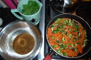 Vegetable mixture in pan with bowl of orange sauce and bowl of spinach.