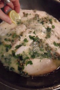 squeezing lemon on the completed fish in pan.