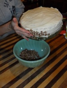 Putting nuts on the side of the frosted cake.