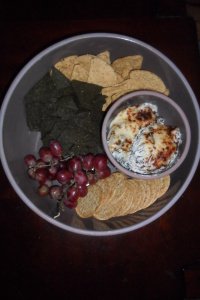 Bowl of dip surrounded by chips, grapes, and crackers.