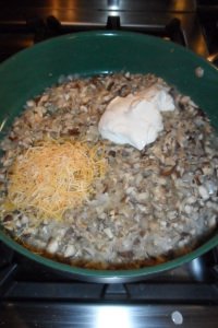 Adding cheese and sour cream to mushrooms.