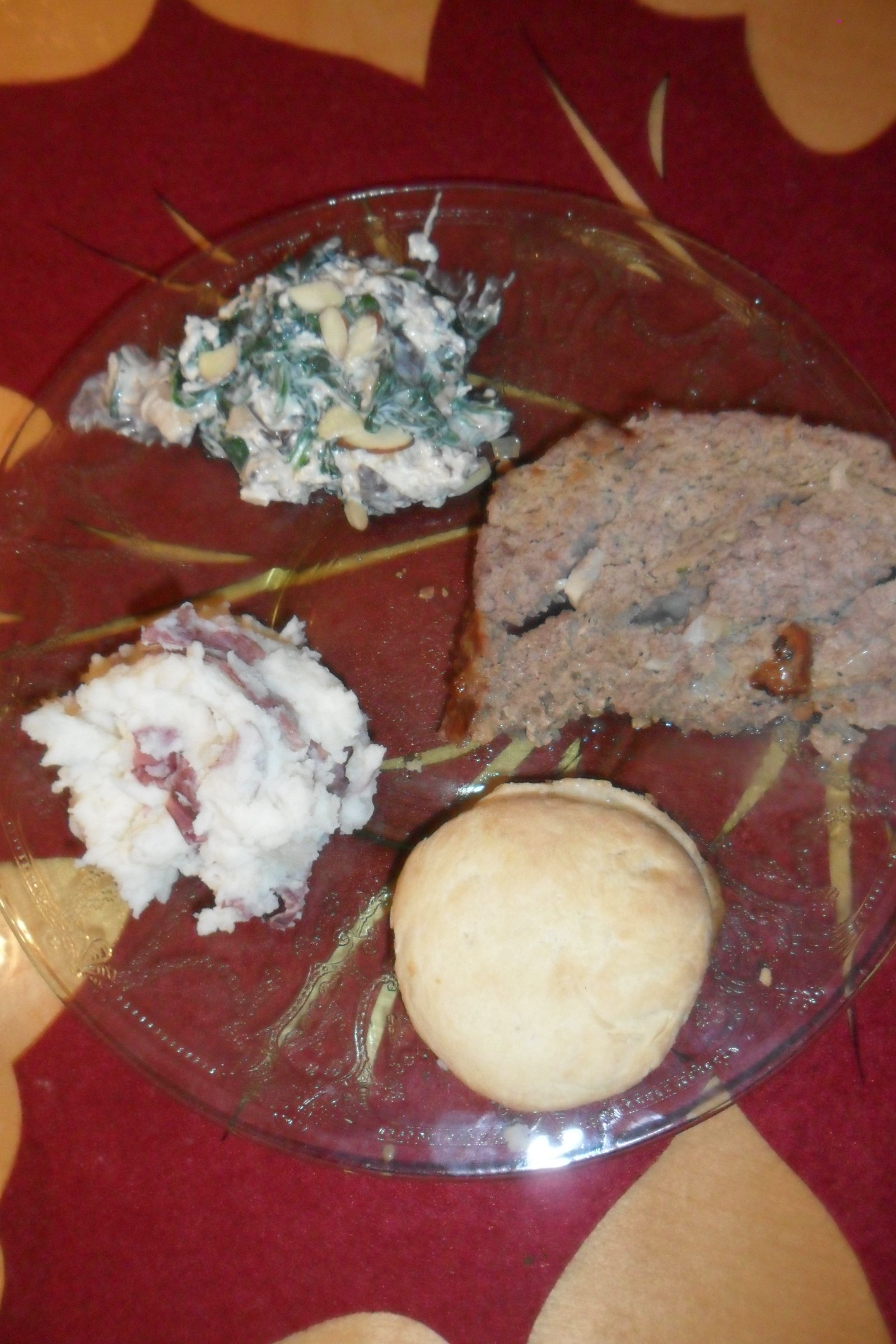 Serving meatloaf with creamed spinach, potatoes, and a biscuit.