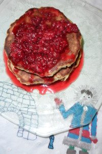 Stack of pancakes covered in berry syrup on eskimo towel.