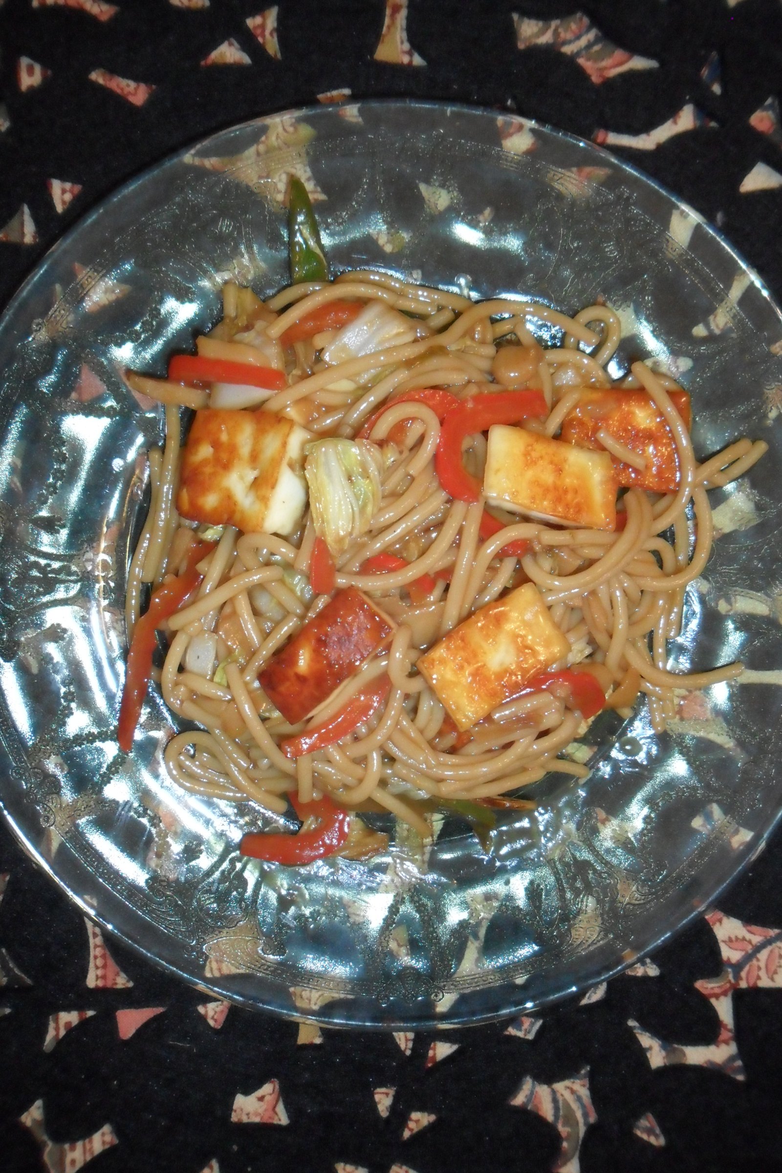 Serving teriyaki paneer on clear plate over Indian cloth.