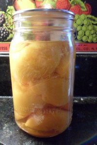 Jar of canned peaches in front of old tin ad.