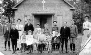 brick schoolhouse with class out front.